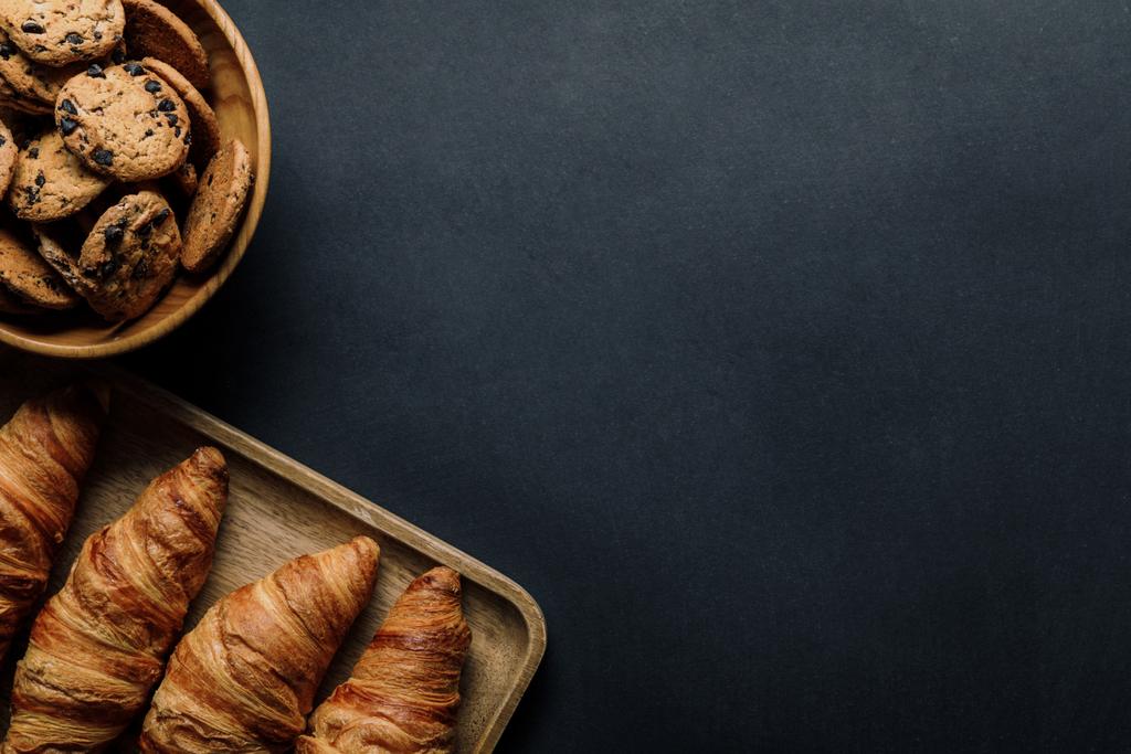 vista elevada da bandeja com deliciosos croissants e biscoitos na tigela na mesa preta
 - Foto, Imagem