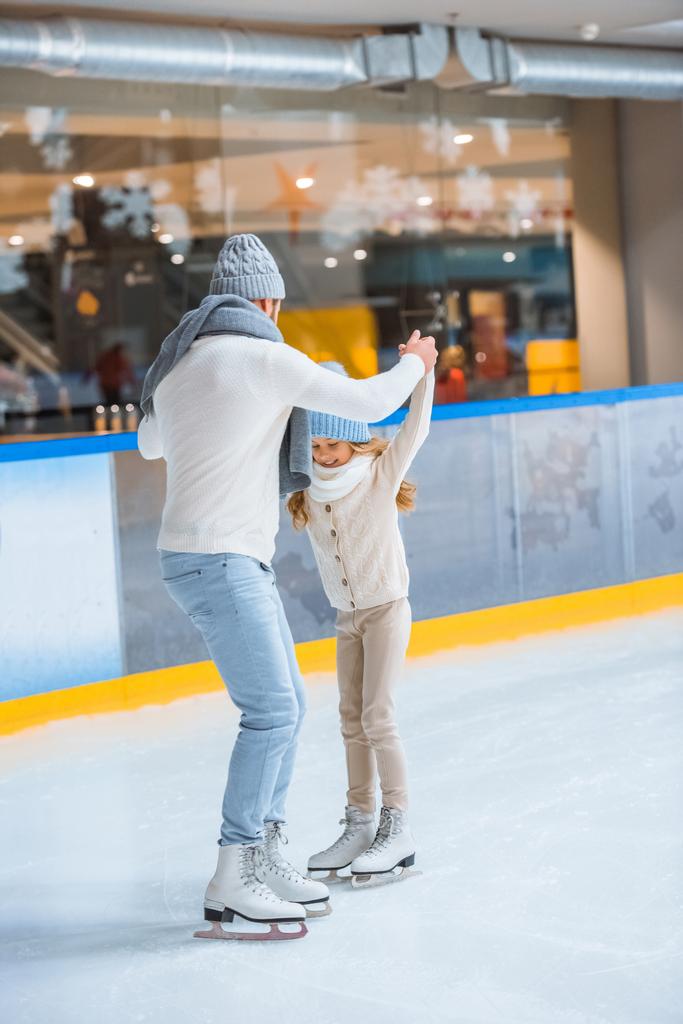 father and daughter in knitted sweaters skating on ice rink together - Photo, Image