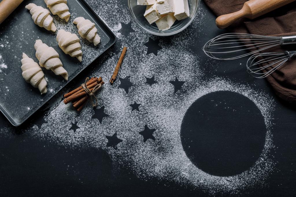Draufsicht auf Tablett mit Croissants, Zutaten und Schneebesen auf Tisch mit Mehl bedeckt mit Sternensymbolen - Foto, Bild