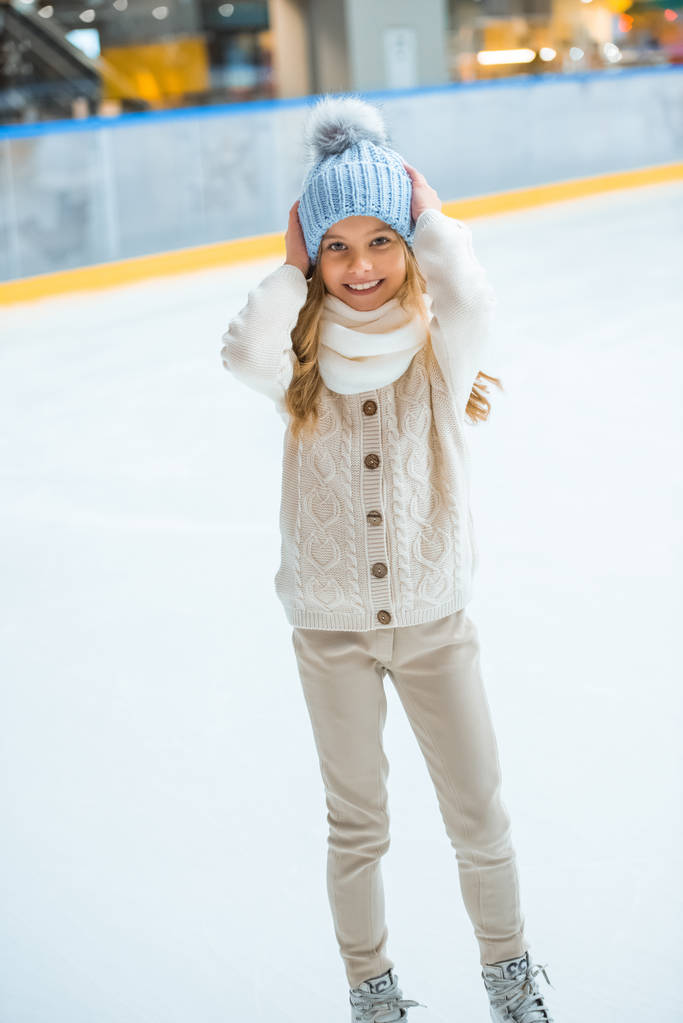 χαμογελώντας αξιολάτρευτο παιδί πουλόβερ και καπέλο σε παγοδρόμιο - Φωτογραφία, εικόνα