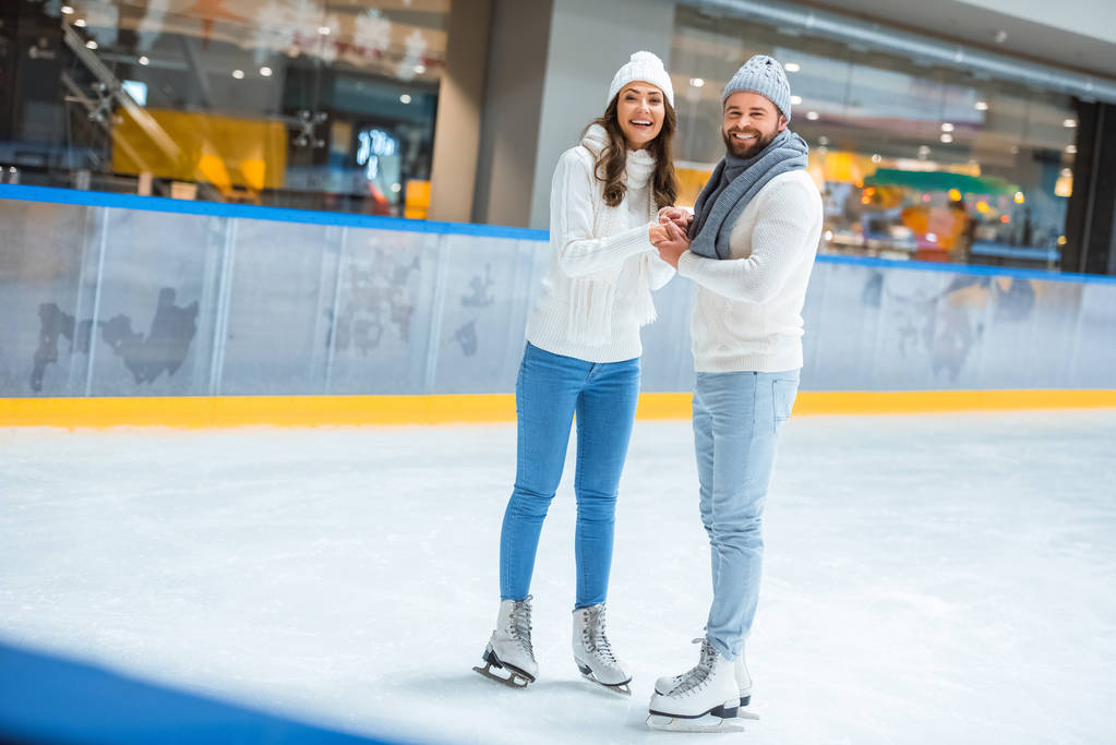 smiling couple in knitted hats and sweaters on skating rink - Photo, Image