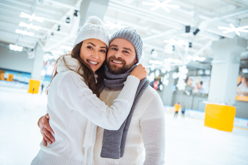 Porträt eines glücklichen Paares, das sich auf der Eisbahn umarmt und in die Kamera blickt - Foto, Bild