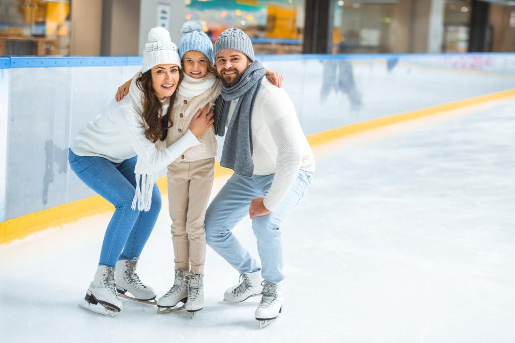 Gut gelaunte Eltern und Tochter in Pullovern blicken auf Eisbahn in die Kamera - Foto, Bild