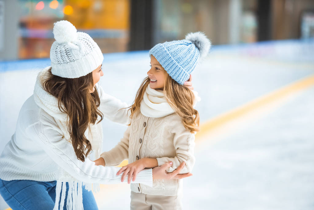 side view of happy mother and daughter looking at each other on skating rink - Photo, Image