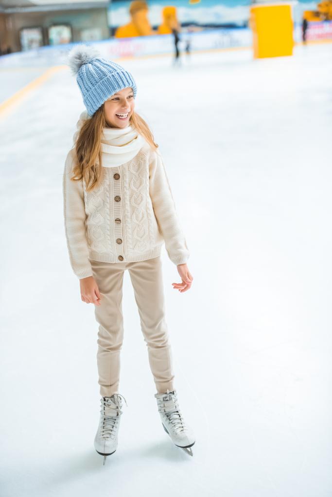 niño alegre en suéter y patines mirando hacia otro lado en pista de patinaje
 - Foto, Imagen