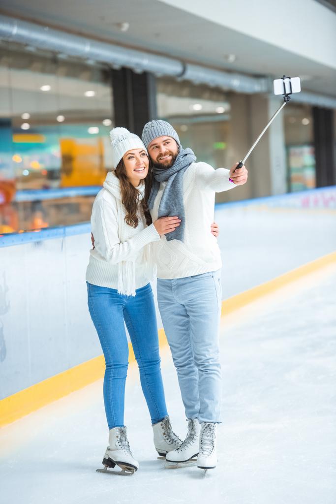 Fröhliches Paar macht gemeinsam Selfie auf dem Smartphone und verbringt Zeit auf der Eisbahn - Foto, Bild