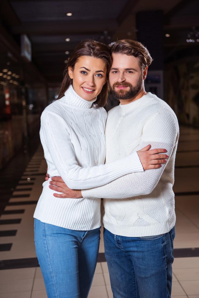 sonriente pareja en suéteres blancos abrazando y mirando a la cámara
 - Foto, imagen