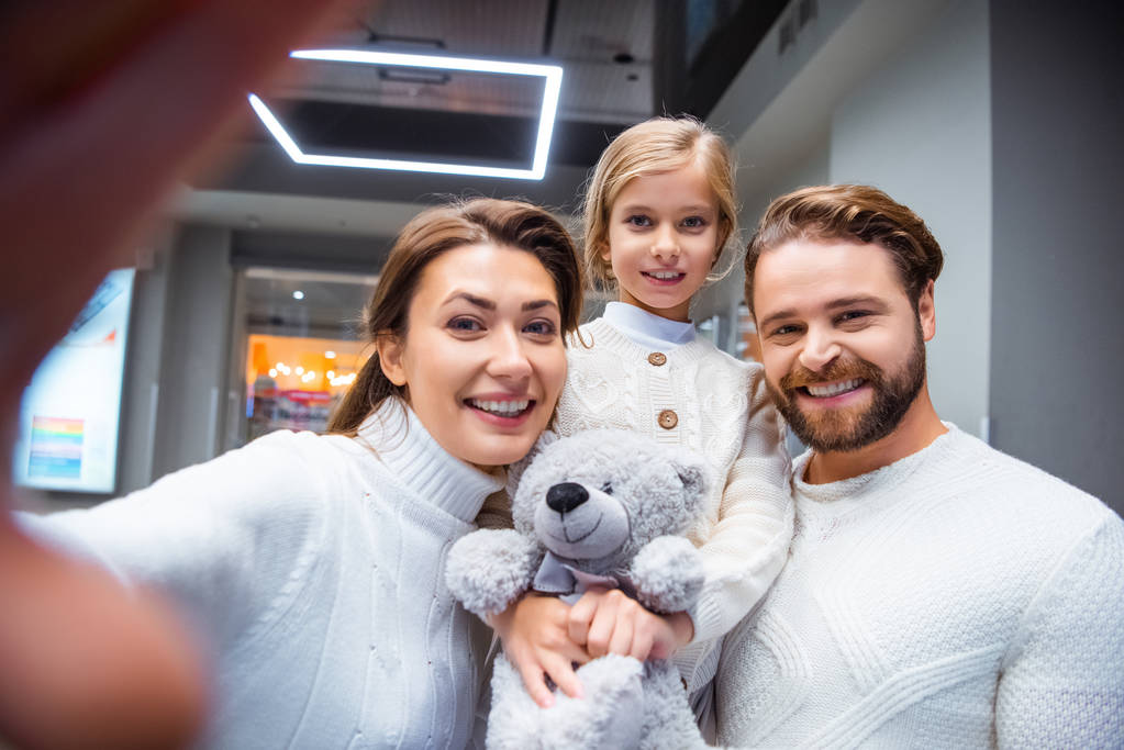 camera point of view of cheerful family in white sweaters taking selfie together - Photo, Image