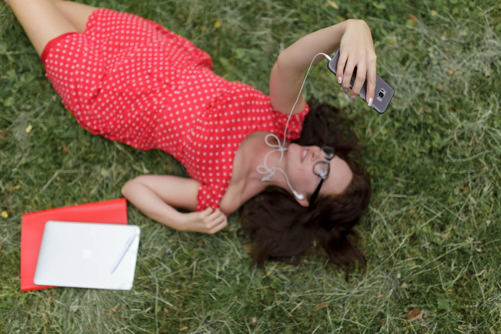 Красива жінка бере селфі, лежачи на траві навколо своїх паперів. Вид зверху
 - Фото, зображення