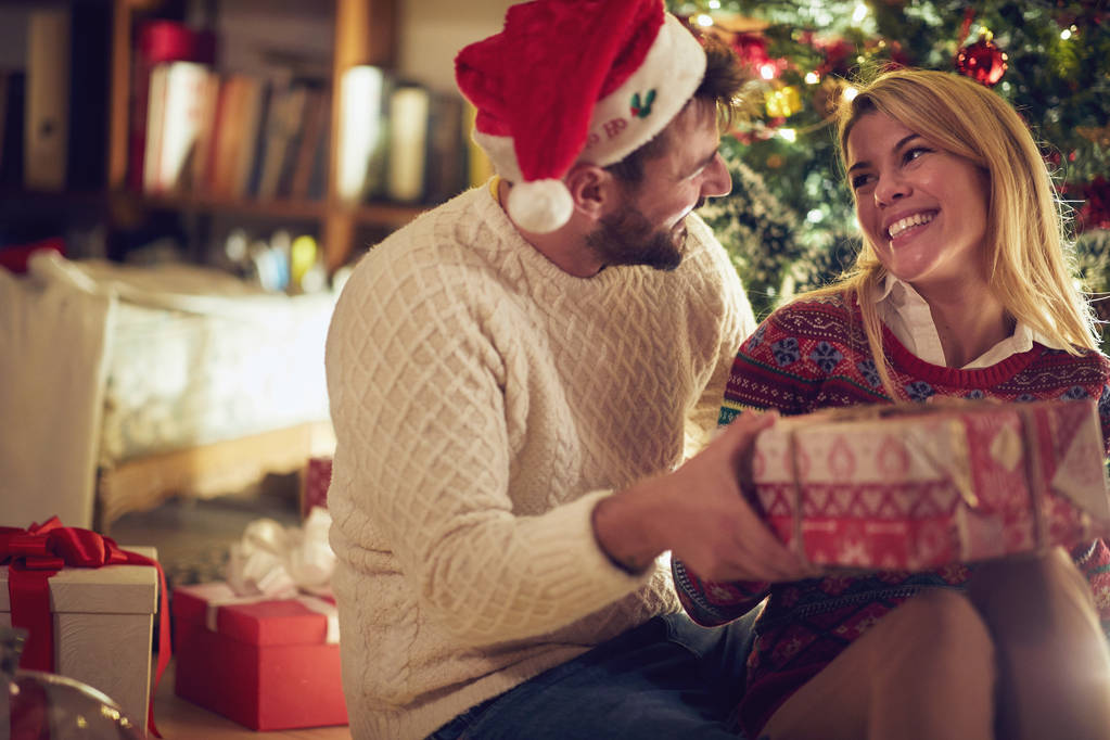 pareja sonriente con regalo y sombrero de Santa Claus por árbol de navidad
 - Foto, Imagen
