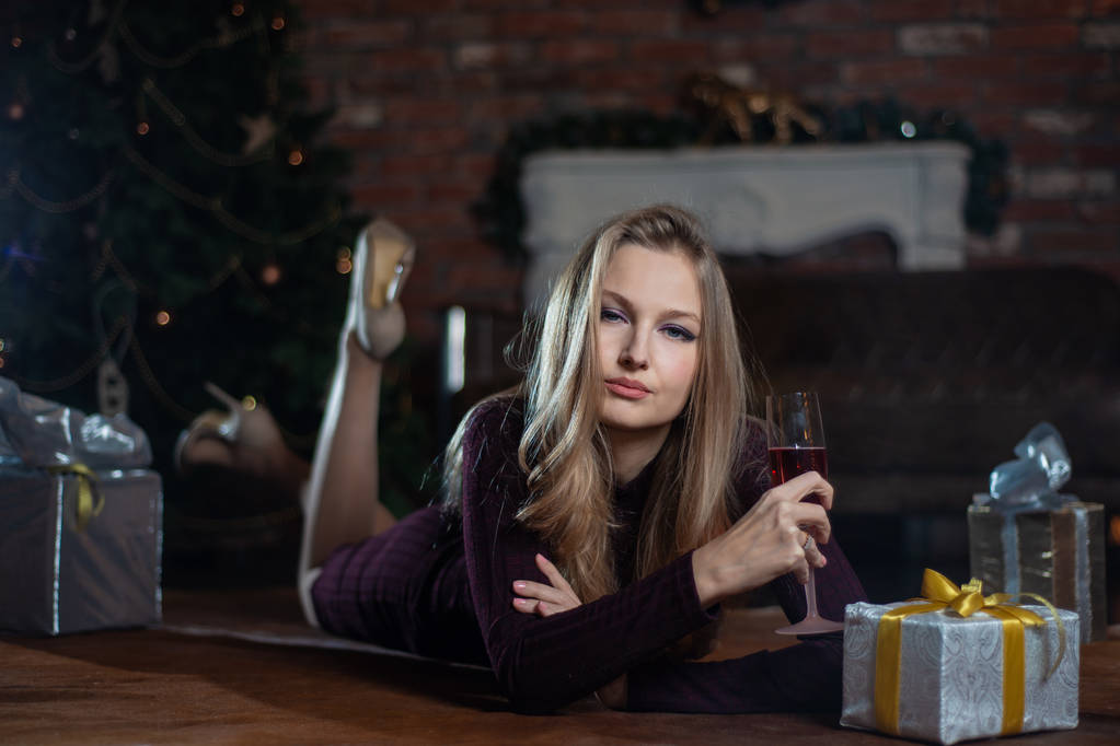 Hermosa joven con un vestido rojo tirado en el suelo con regalos y champán cerca del árbol de Navidad
 - Foto, imagen