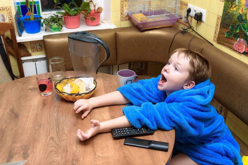 Каждый день в центре внимания семьи: портрет веселого счастливого милого белого ребенка 7 лет на кухне, обедающего дома за завтраком. Он прямо перед камерой в различных позах
. - Фото, изображение