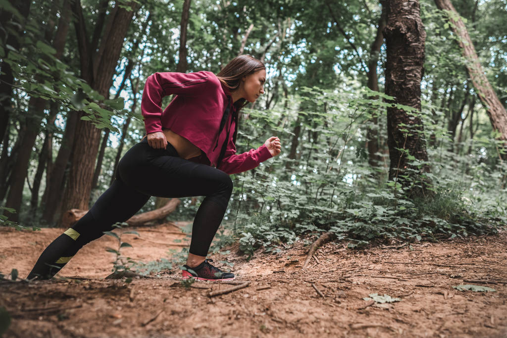 Μερική άποψη του ένα νεαρό κορίτσι σπορ υπερνικά απότομες αναβάσεις στην κατάρτιση στο δάσος. Πλήρες μήκος βολή του αυτοπεποίθηση αθλήτρια αναρρίχηση ένα μονοπάτι του δάσους. - Φωτογραφία, εικόνα