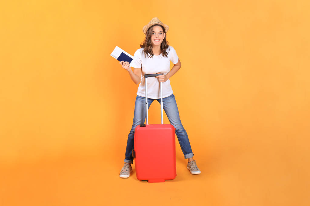 Joven turista en ropa casual de verano, con maleta roja, pasaporte, entradas aisladas sobre fondo beige
. - Foto, Imagen