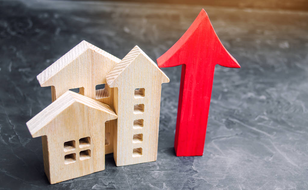 Holzhäuser mit einem roten Pfeil nach oben. Konzept der hohen Nachfrage nach Immobilien. Steigerung der Energieeffizienz von Wohnungen. Anstieg der Häuserpreise. Eigentum. Bevölkerungswachstum. Zunahme auf dem Immobilienmarkt - Foto, Bild