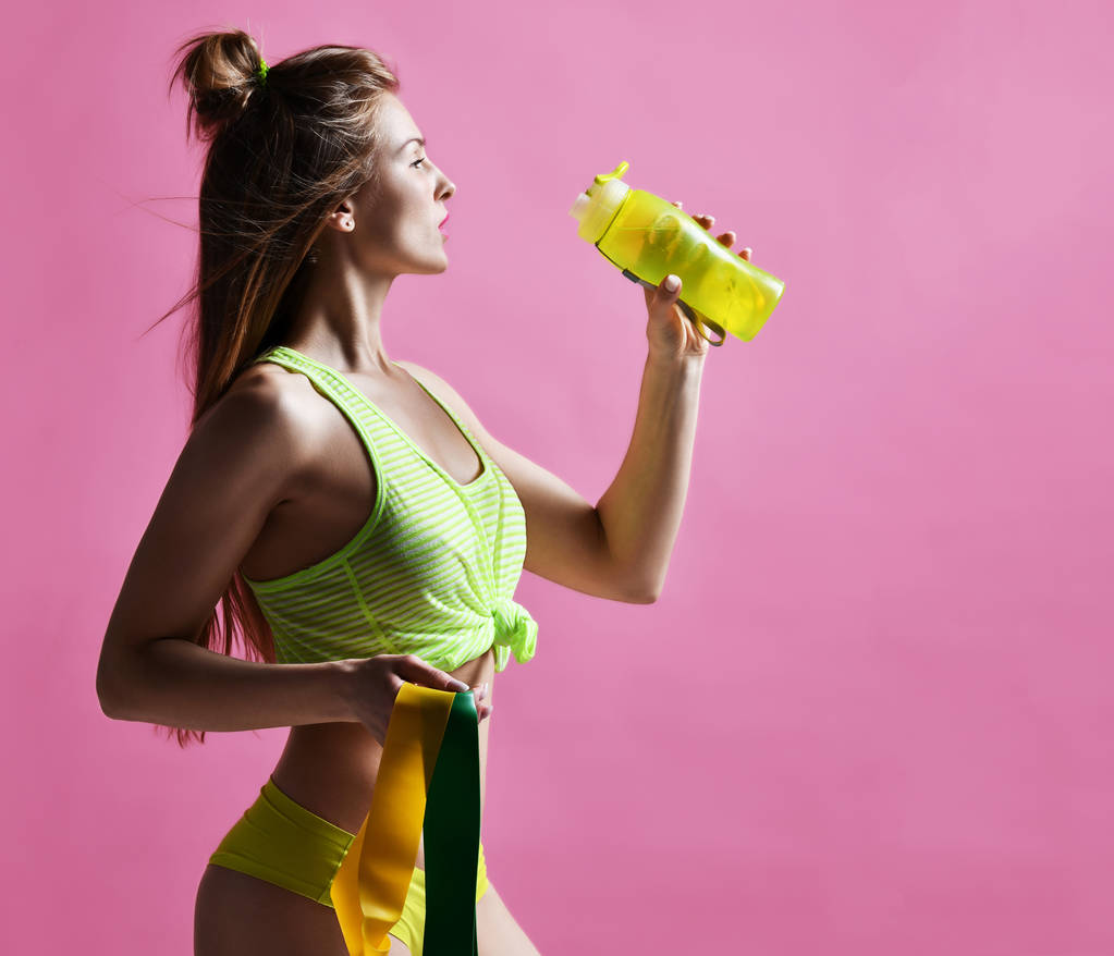 Молода спортивна жінка з питною пляшкою з водою і зелену і жовту гумову розтяжку
 - Фото, зображення