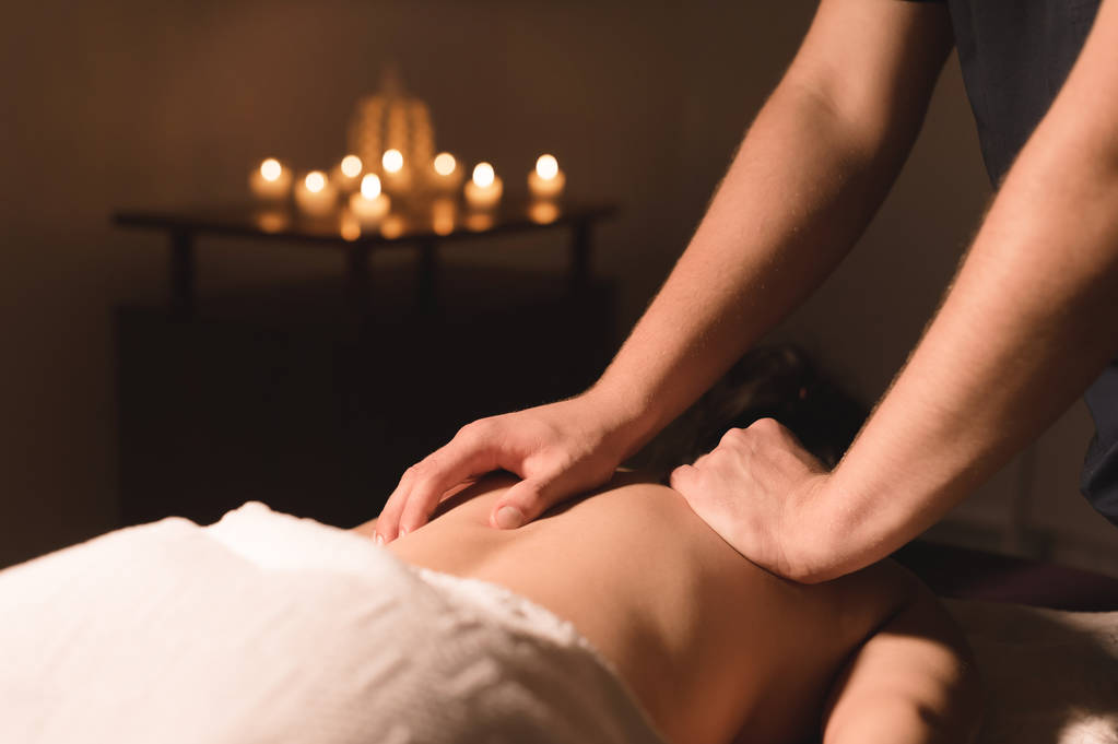 Gros plan mains masculines faisant massage curatif à l'huile à une jeune fille dans un bureau de cosmétologie sombre. Clé sombre
 - Photo, image