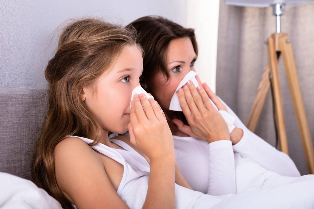 Matka a dcera trpí studené foukání jí nos kapesníkem na posteli - Fotografie, Obrázek