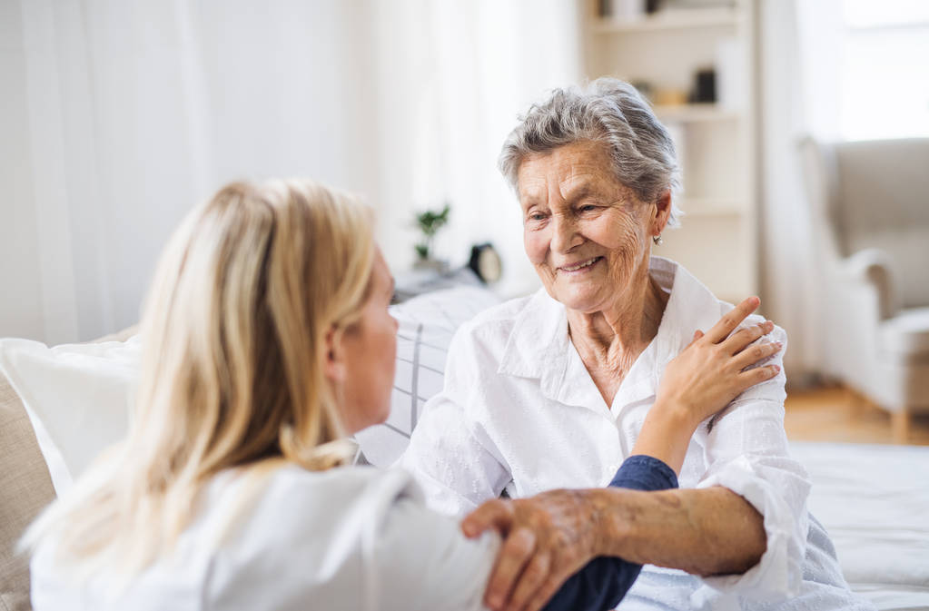 Um visitante de saúde conversando com uma mulher idosa doente sentada na cama em casa
. - Foto, Imagem