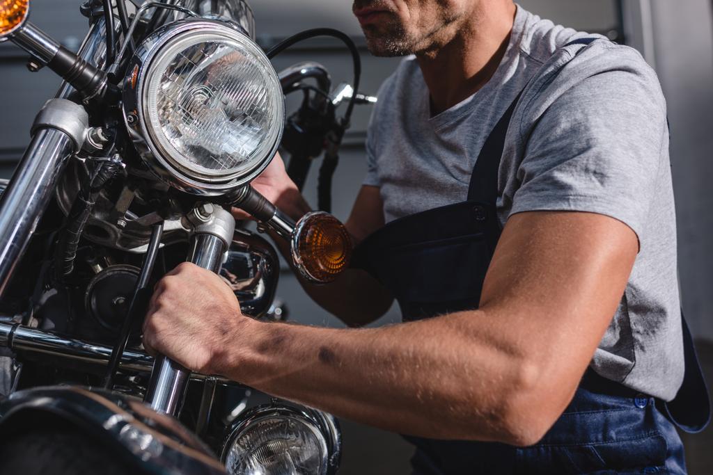 Ausgeschnittene Ansicht eines Mechanikers, der Motorradscheinwerfer in der Garage befestigt - Foto, Bild