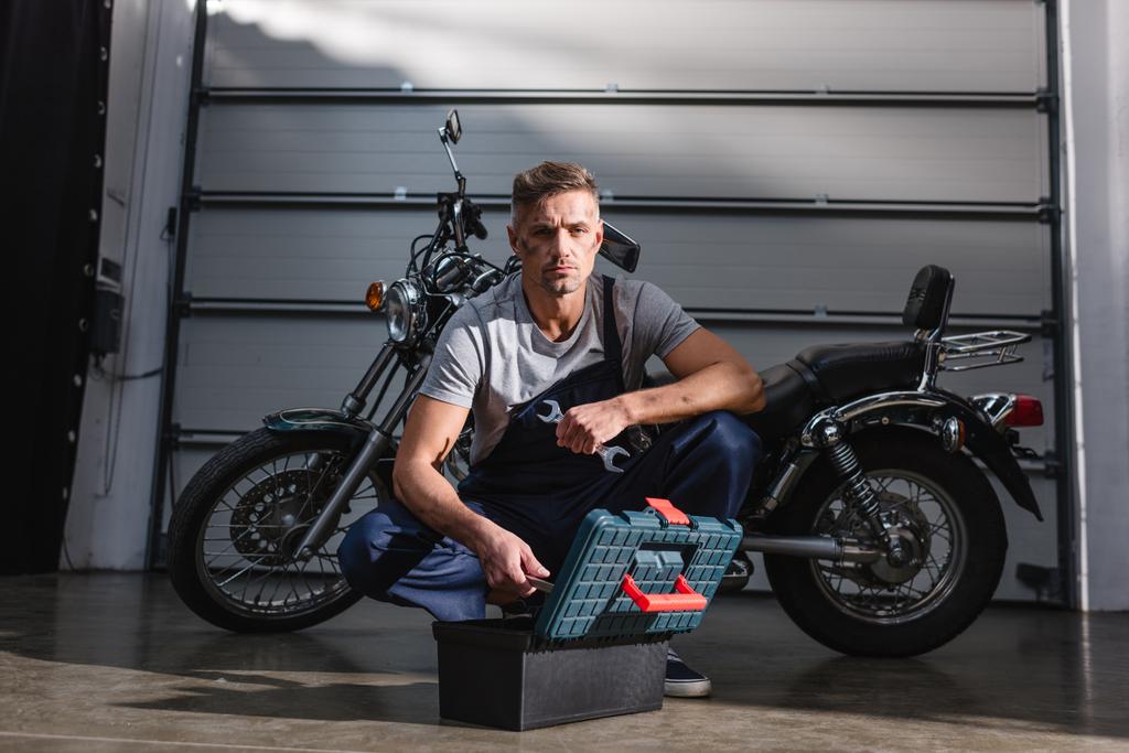 guapo mecánico enfocado tomar llaves de caja de herramientas para la fijación de la motocicleta en el garaje
 - Foto, Imagen