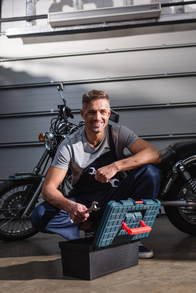 mécanicien souriant prendre des clés de la boîte à outils pour fixer la moto dans le garage
 - Photo, image