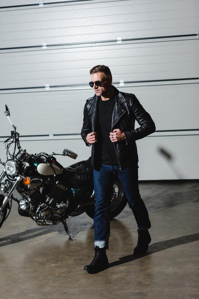 cool guy in sunglasses and leather jacket walking in garage - Photo, Image