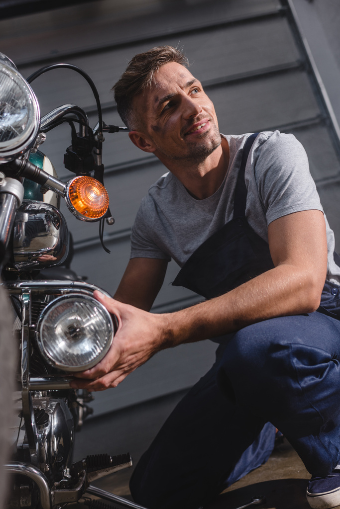 hymyilevä aikuinen mekaanikko vahvistamisesta moottoripyörän ajovalaisin autotallissa
 - Valokuva, kuva