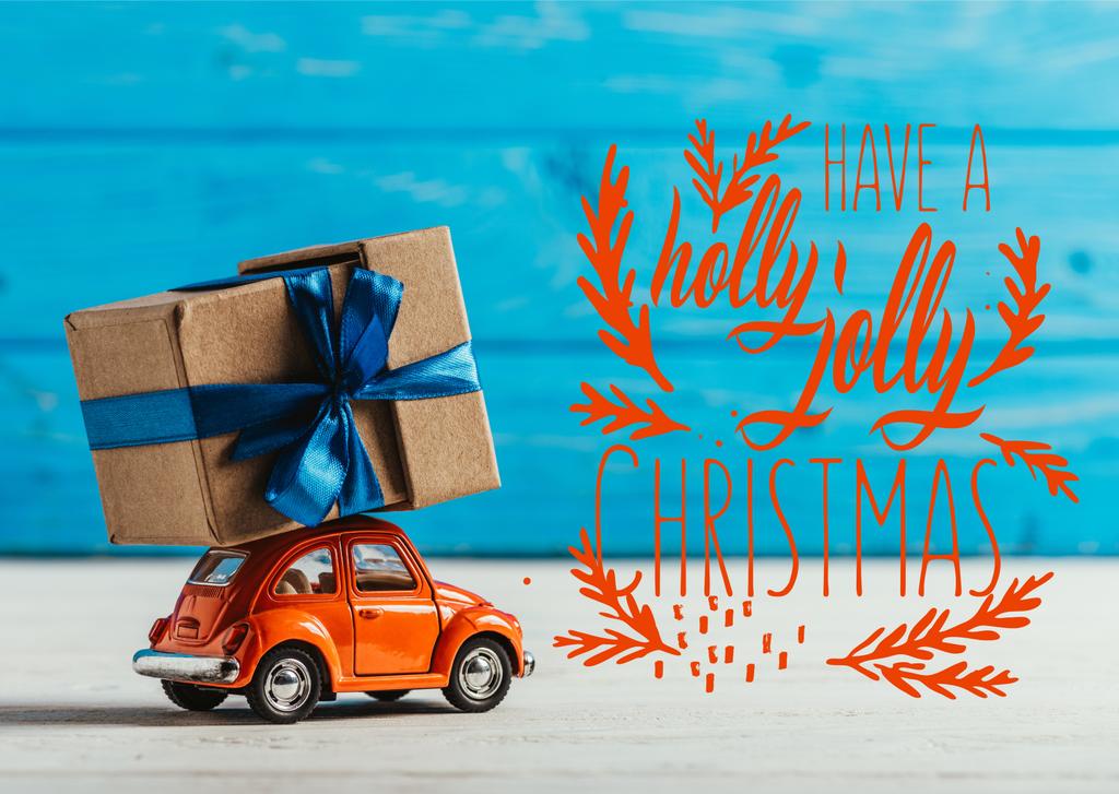 primer plano de coche de juguete con caja de regalo sobre fondo de madera azul con inspiración "have a holly jolly christmas"
 - Foto, Imagen
