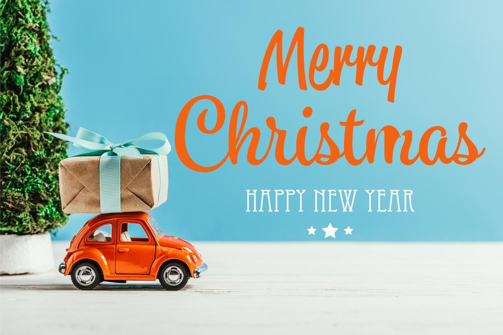 Close-up shot van speelgoed voertuig met de doos van de gift op blauwe achtergrond met "merry christmas and happy new year" belettering - Foto, afbeelding