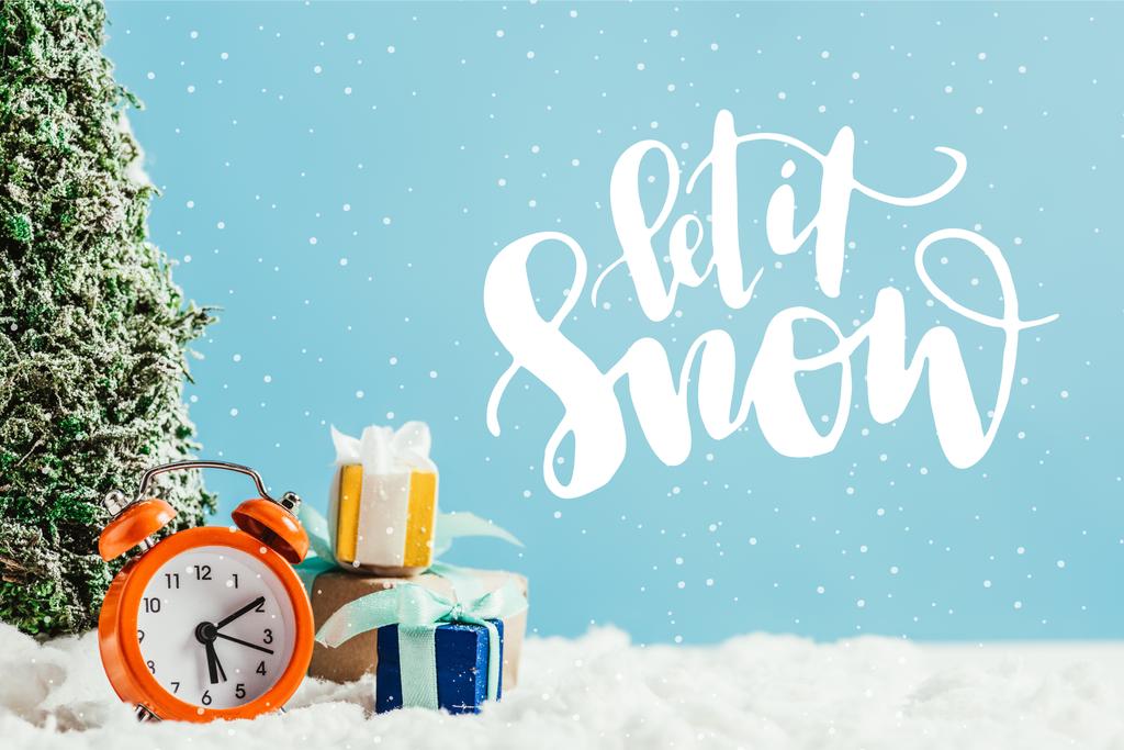 primo piano di regali di Natale con sveglia e albero di Natale in miniatura in piedi sulla neve su sfondo blu con scritte "lascia che nevichi"
 - Foto, immagini