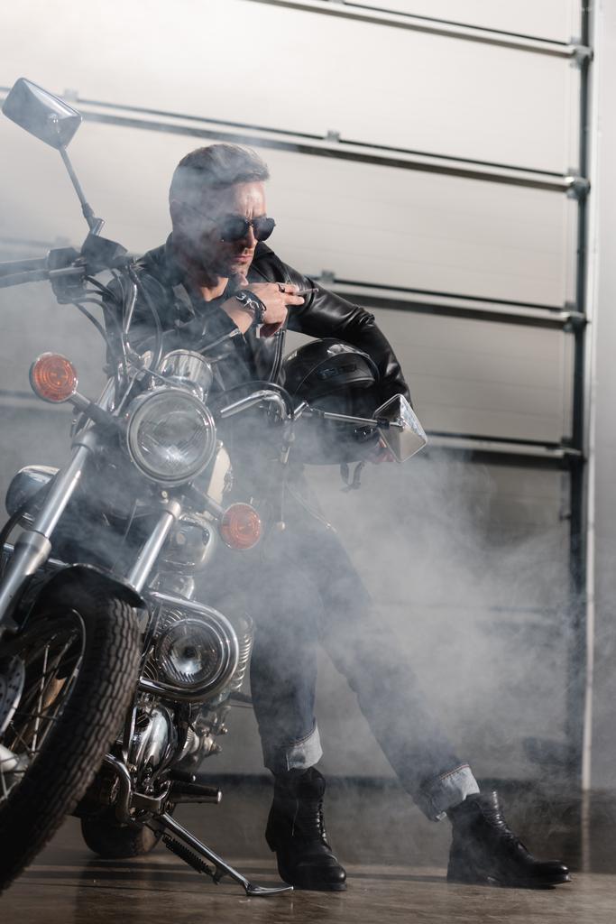 cavaleiro bonito em óculos escuros pretos encostados na motocicleta na garagem
 - Foto, Imagem