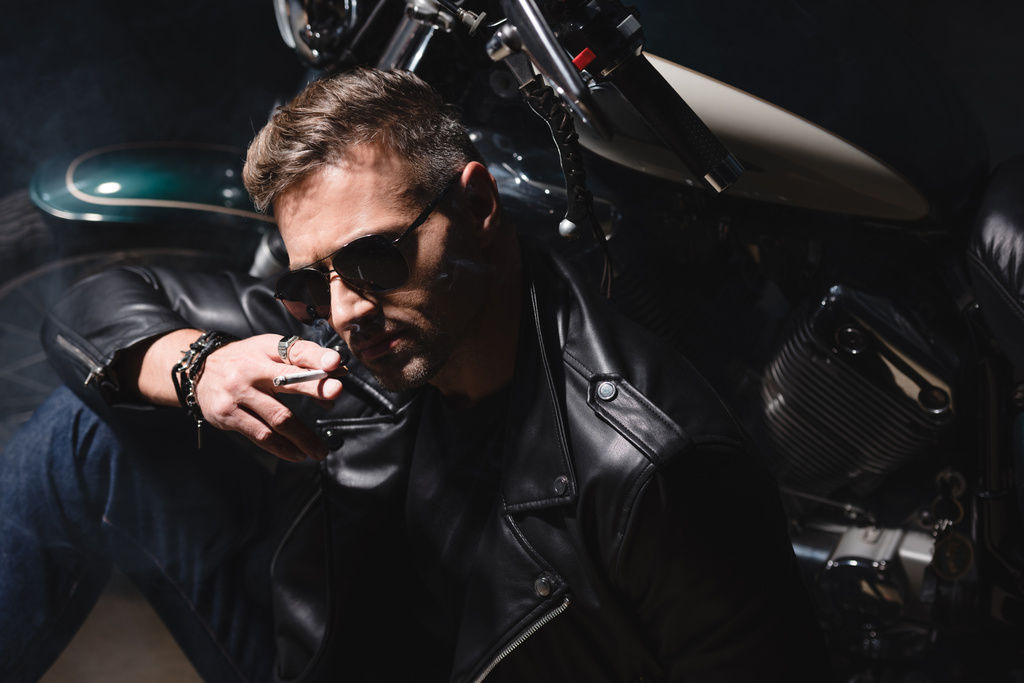 gutaussehender Mann mit Sonnenbrille sitzt mit Motorrad in Garage - Foto, Bild