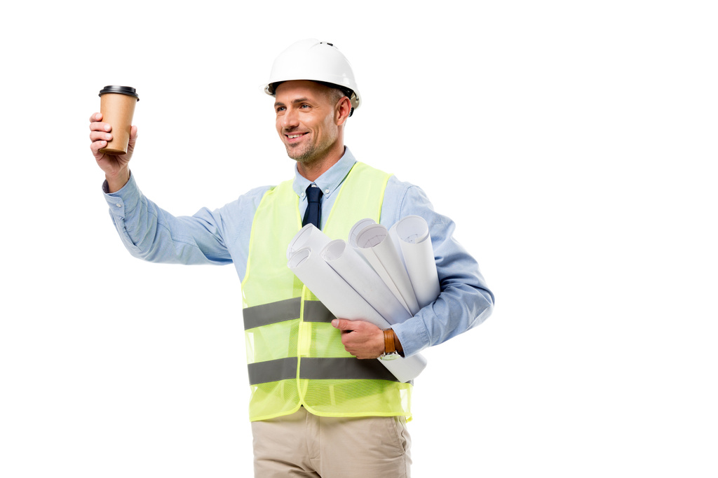 glimlachend ingenieur in veiligheidsvest holding blauwdrukken en koffie gaan geïsoleerd op wit - Foto, afbeelding