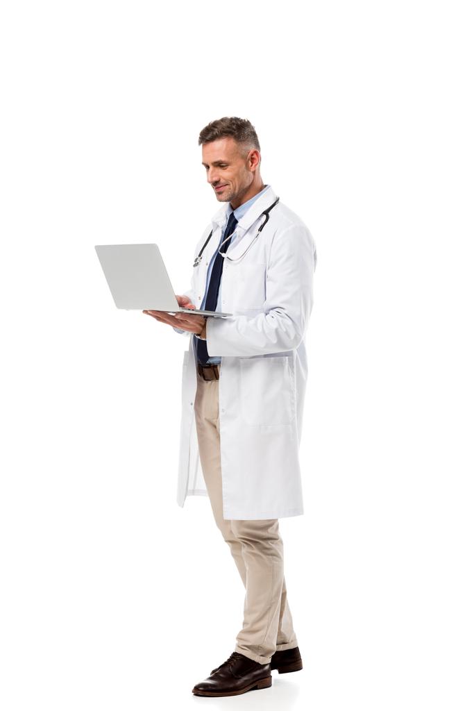 schöner Arzt in weißem Mantel mit Stethoskop mittels Laptop isoliert auf weiß - Foto, Bild