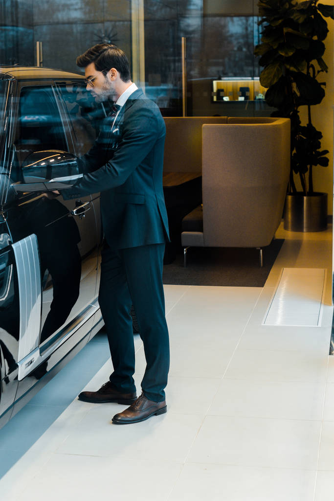 vue latérale de l'homme d'affaires en costume ouvrant la porte de l'automobile noire
 - Photo, image