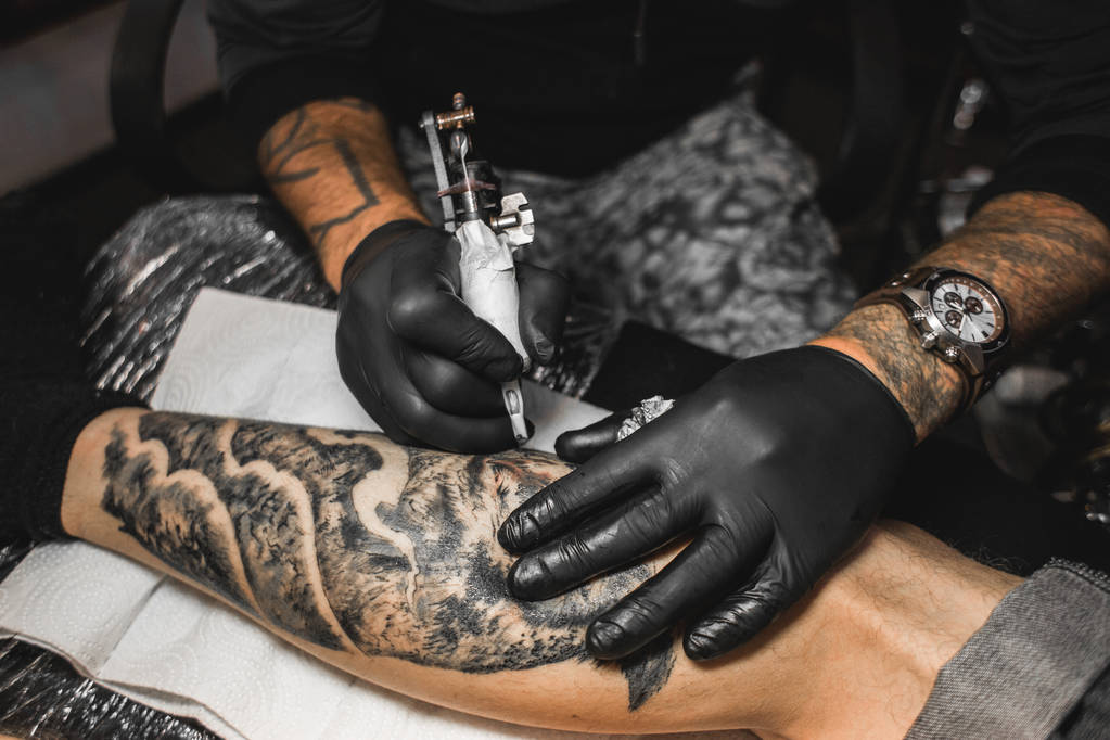 A tetováló művész létrehoz egy képet a test egy ember. közeli kép: tetováló gépek és kezek - Fotó, kép