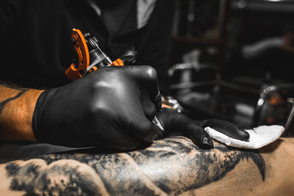 Tattoo umělec vytvoří obrázek na těle muže. Detail tetovací strojky a ruce - Fotografie, Obrázek