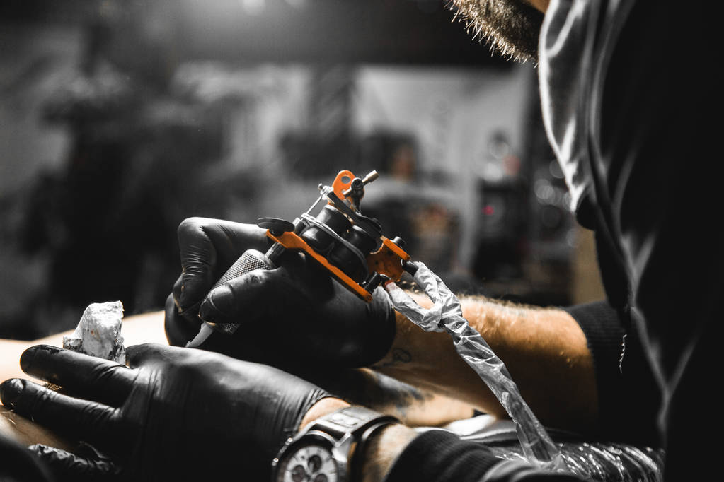 Ο καλλιτέχνης τατουάζ δημιουργεί μια εικόνα στο σώμα ενός ανθρώπου. κοντινό πλάνο τατουάζ μηχανές και τα χέρια - Φωτογραφία, εικόνα