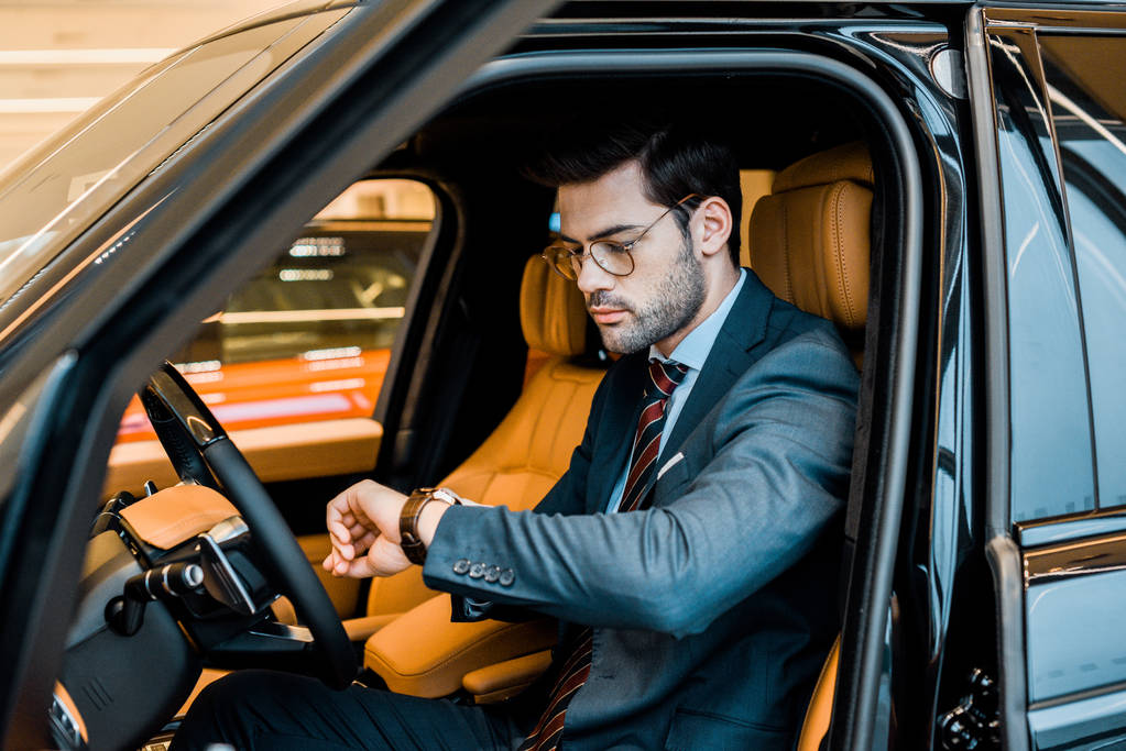 κομψό επιχειρηματία σε γυαλιά έλεγχος ρολόι σε πολυτελές αυτοκίνητο - Φωτογραφία, εικόνα