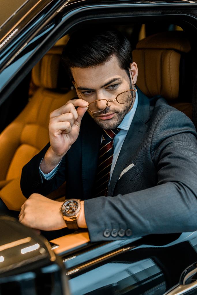 стильний бізнесмен з розкішним годинником, що надягає окуляри, сидячи в машині
 - Фото, зображення
