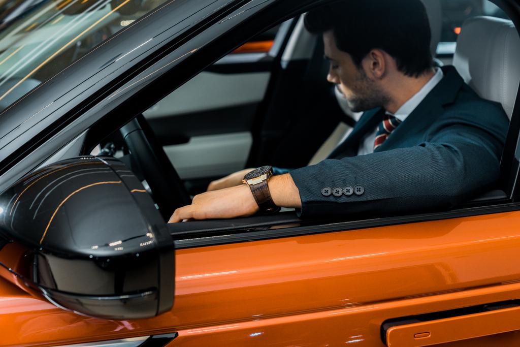 foco seletivo de homem de negócios elegante sentado em carro laranja de luxo
 - Foto, Imagem