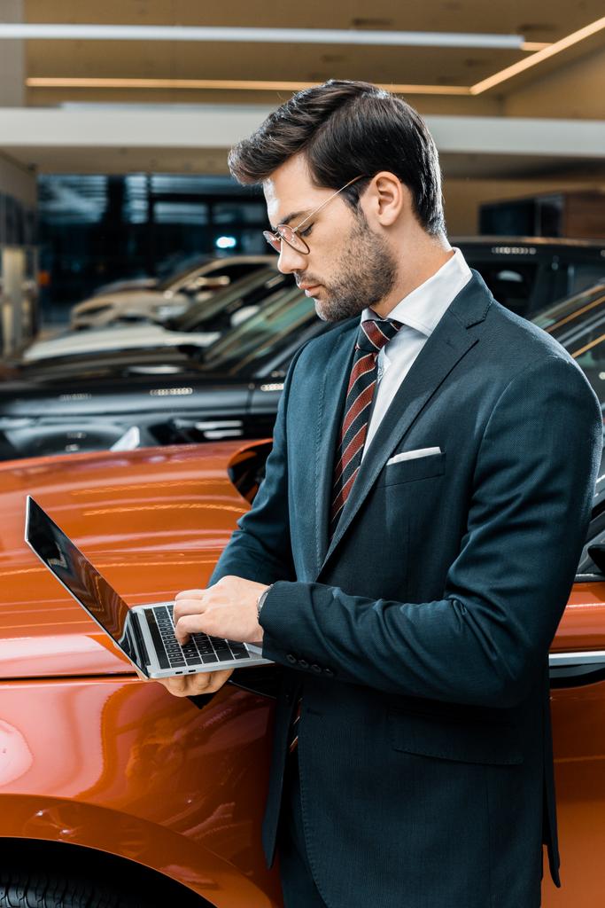 вид збоку бізнесмена в окулярах, використовуючи ноутбук біля автомобіля
  - Фото, зображення