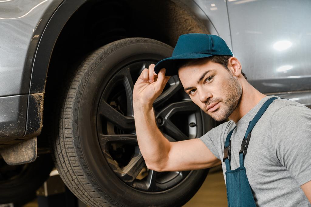 portrait of male auto mechanic in working overall posing near car at repair shop - Photo, Image