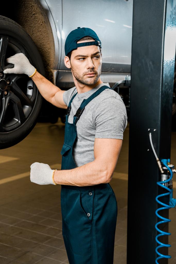 自動車修理店で自動車に立って保護手袋で若い自動車整備士 - 写真・画像