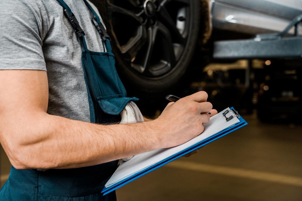 cropped shot of repairman with notepad checking car wheels at auto repair shop - Photo, Image