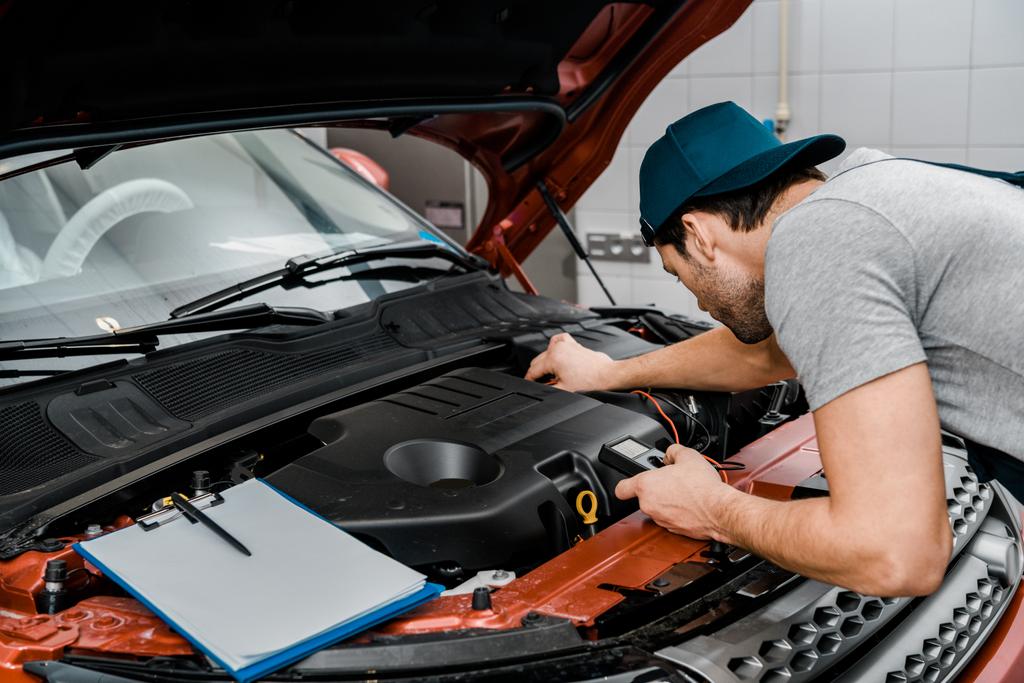 Automechaniker mit Multimeter-Voltmeter überprüfen Autobatteriespannung im Mechaniker-Geschäft - Foto, Bild