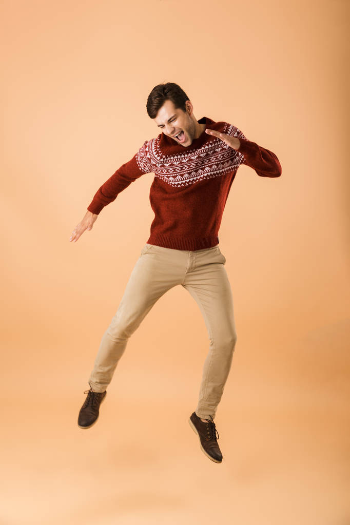 Image pleine longueur d'homme non rasé 20s avec soies portant pull tricoté riant et se réjouissant isolé sur fond beige
 - Photo, image
