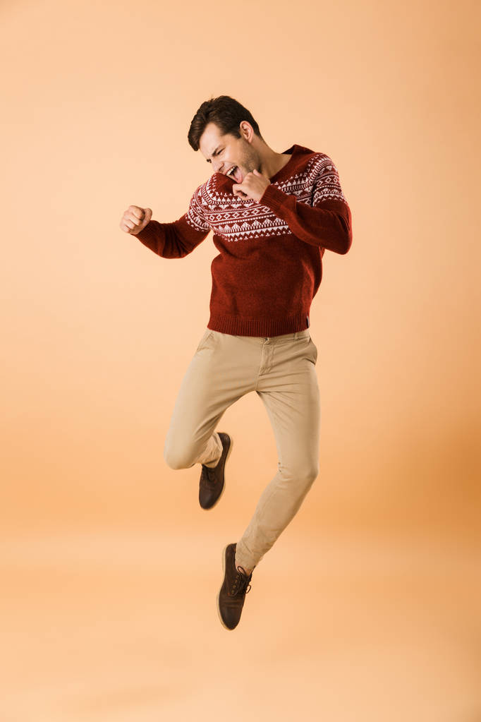Imagen de larga duración del hombre alegre de 20 años con cerdas que usan suéter de punto gritando de felicidad aislado sobre fondo beige
 - Foto, imagen