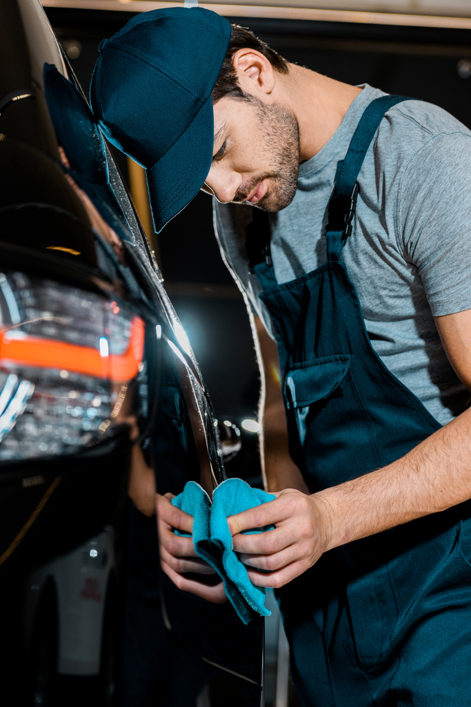 Jeune auto mécanicien nettoyage voiture avec chiffon à l'atelier de réparation automobile
 - Photo, image